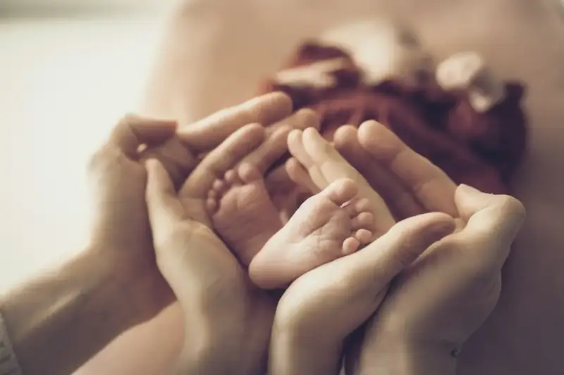 Parents’ hands gently holding their baby’s feet